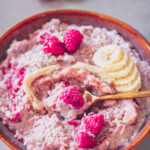 Veganes Kokos-Milchreis-Porridge mit Himbeeren, Banane und geschmolzener weißer Schokolade